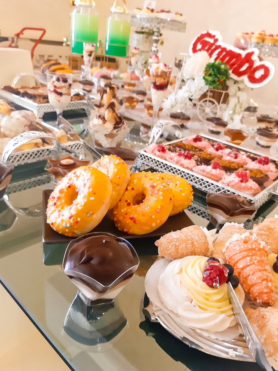 Masă dulce de eveniment pregătită de Cofetăria Giumbo, cu gogoși glazurate, cannoli și prăjituri, pe suport oglindă